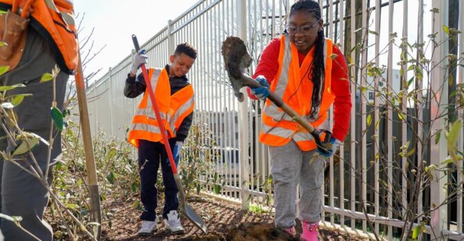 Two students dig a hole as they learn how trees are planted