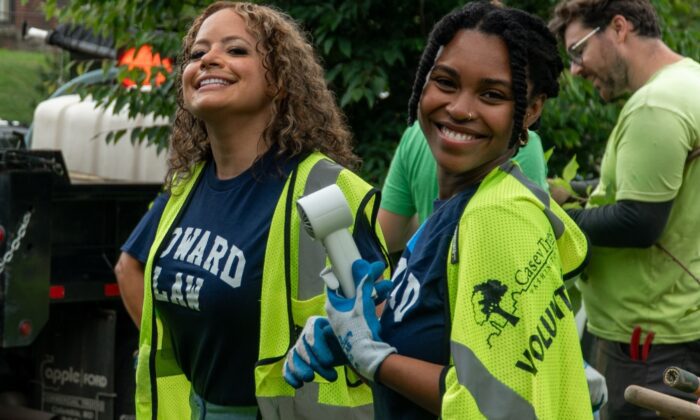 Two incoming Howard University Law students smile for the camera in front of a truck filled with mulch. Other students and Casey Trees employees work in the background.