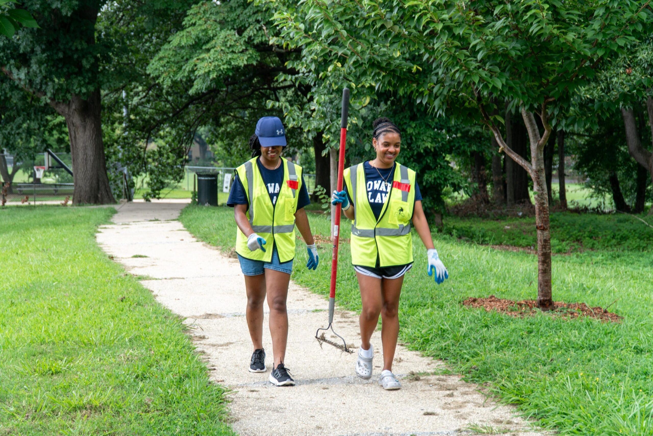 Two incoming Howard University Law students smile as they walk back from caring for a young tree. One student is holding a rake.