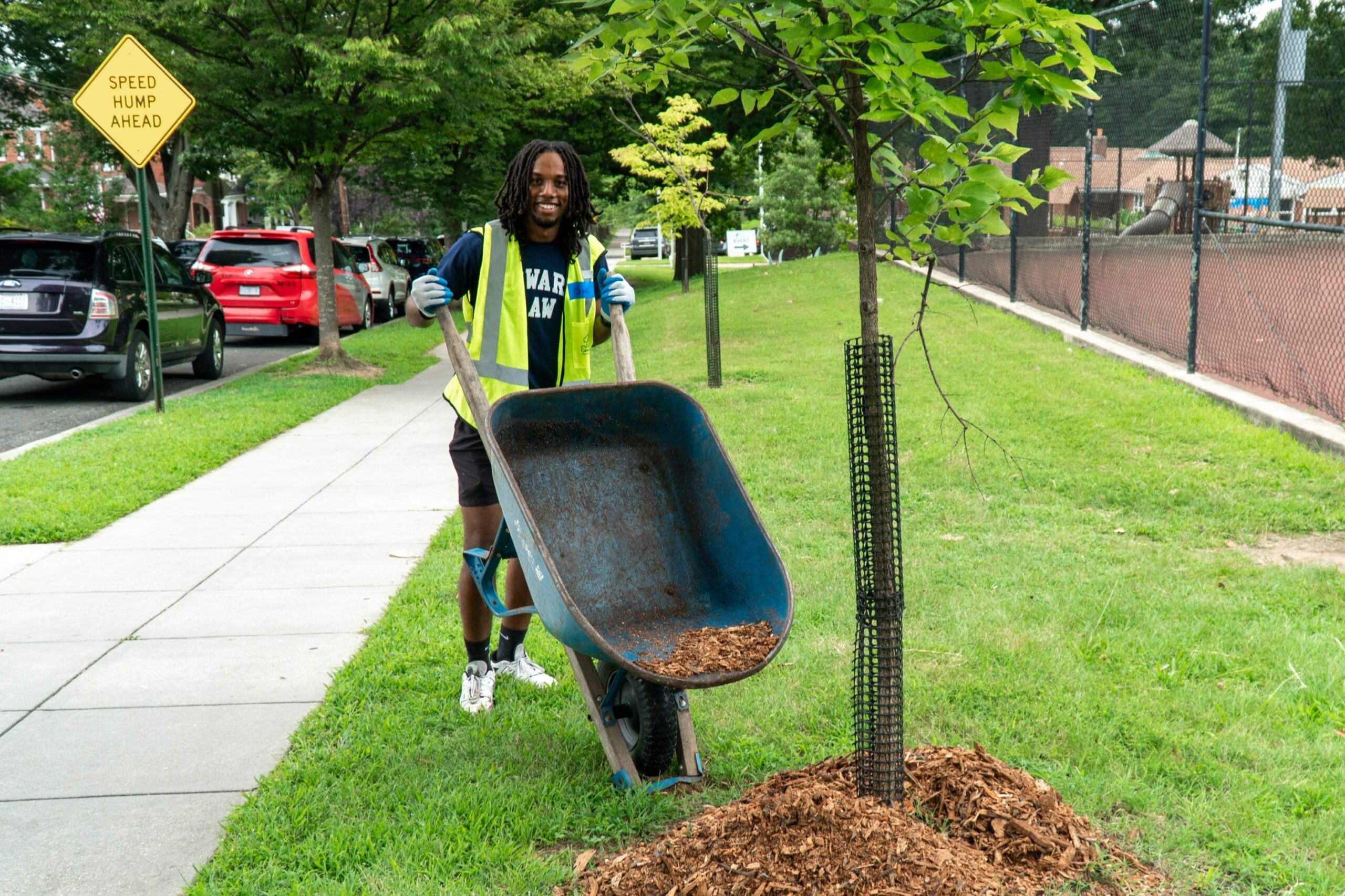 An incoming Howard University Law student smiles for the camera as they dump mulch from a wheelbarrow around the base of a young tree.