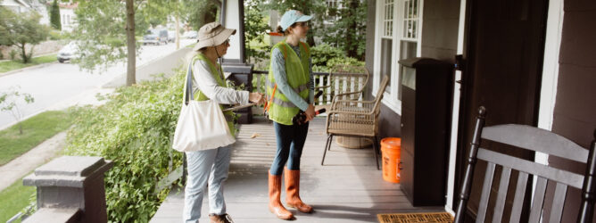 Two volunteers stand on the porch of a house canvassing about invasive vines.