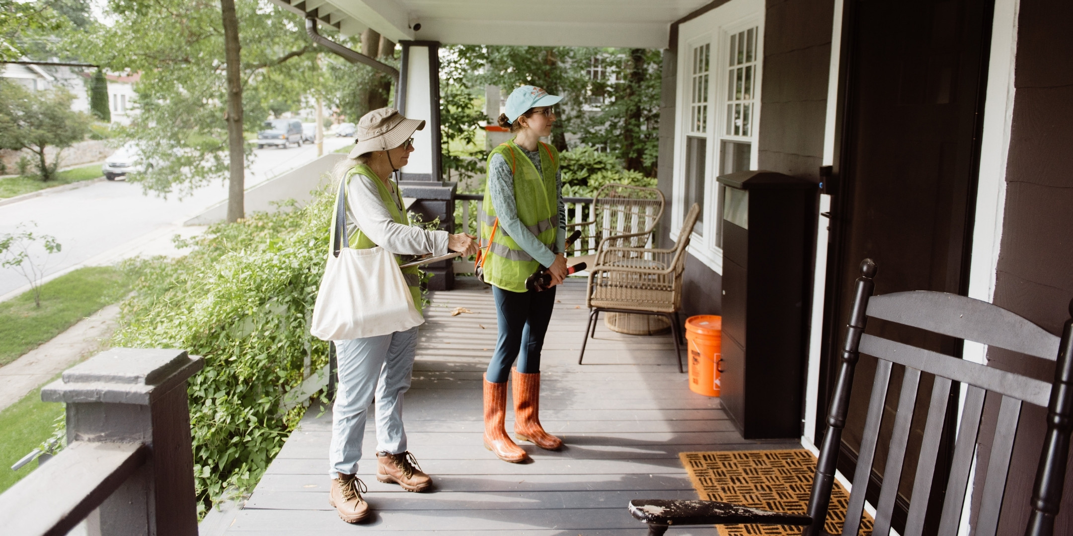 Two volunteers stand on the porch of a house canvassing about invasive vines.