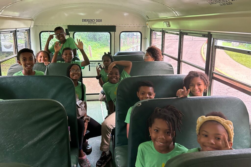 A group of young students smile for the camera as they sit on a school bus.