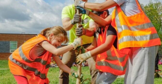A group of children and an adult plant a tree on a school campus