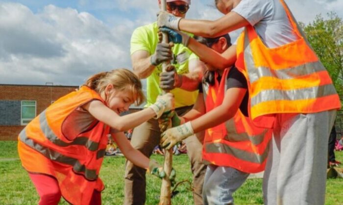 A group of children and an adult plant a tree on a school campus