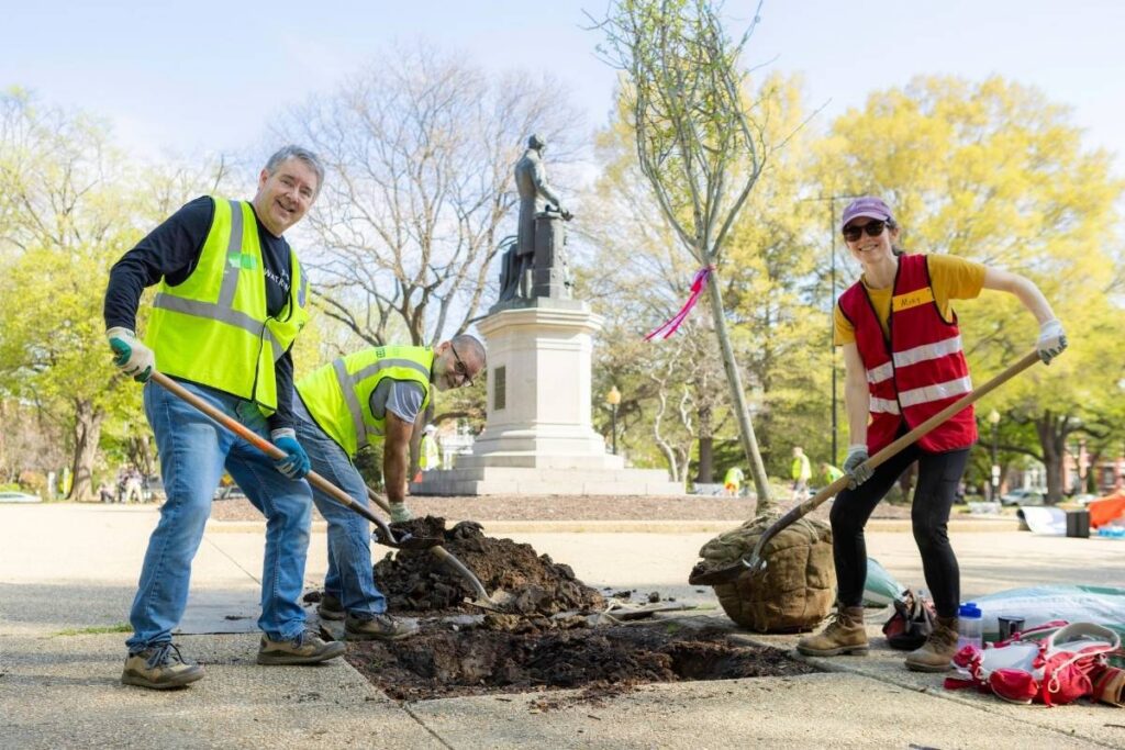 Three volunteers smile for the camera, shovels in hand.