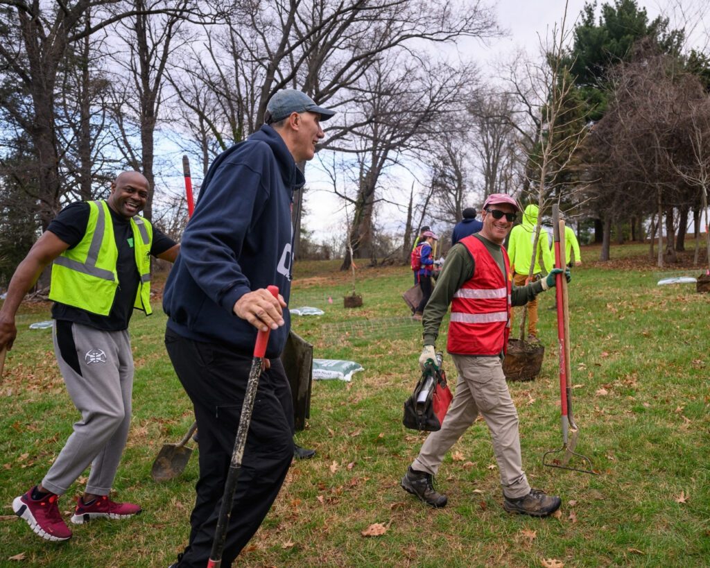 A Team Leader walks with tools with two former Washington Wizards at a Community Tree Planting.