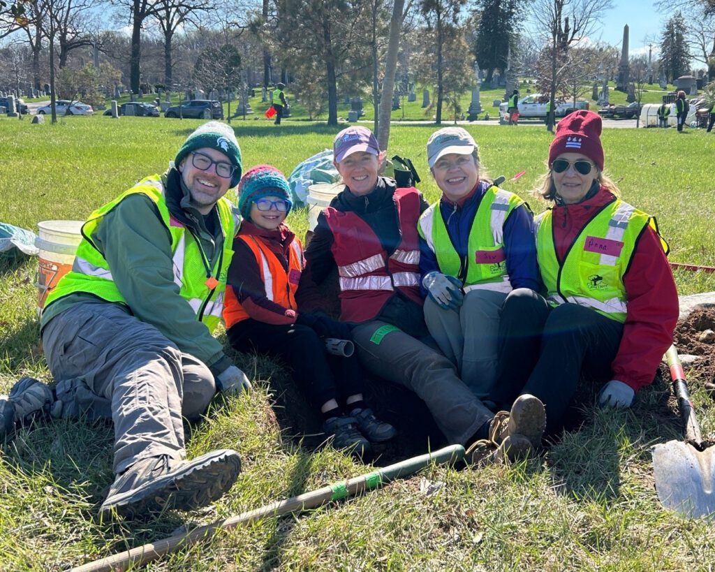 A group of volunteers sit in a freshly-dug hole and smile.