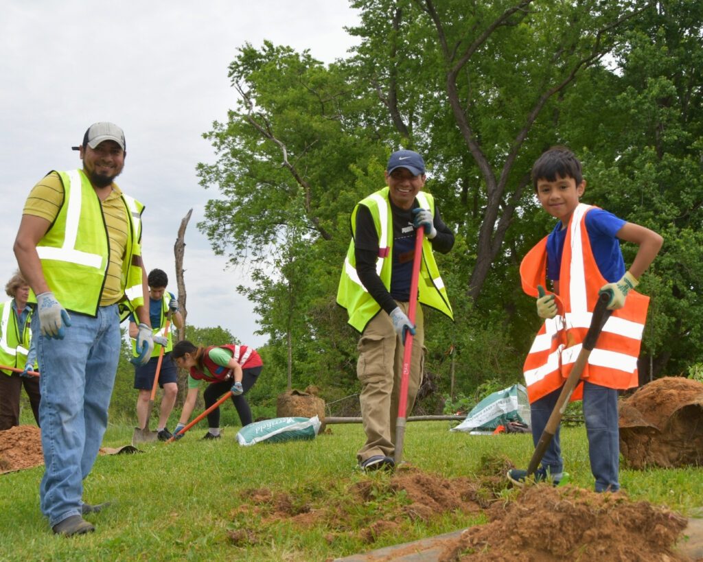 Three volunteers smile as they dig a hole at a Community Tree Planting.