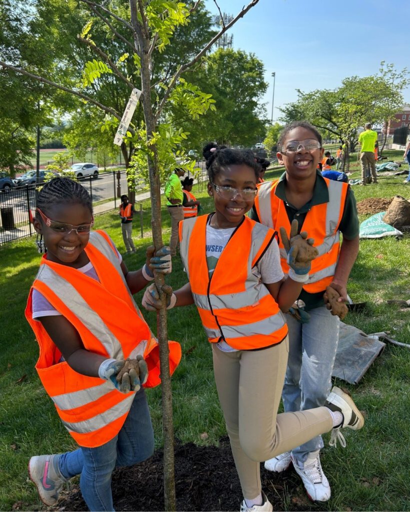 Three students smile next to their newly planted tree.
