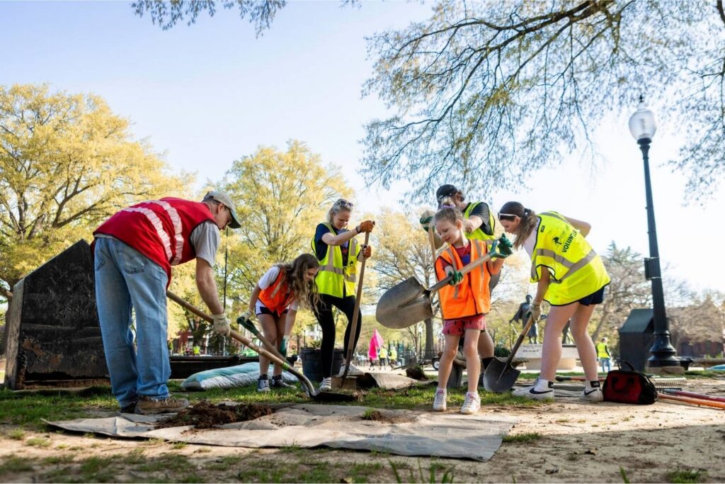A group of volunteers wearing high-vis vests plant a tree at Lincoln Park.