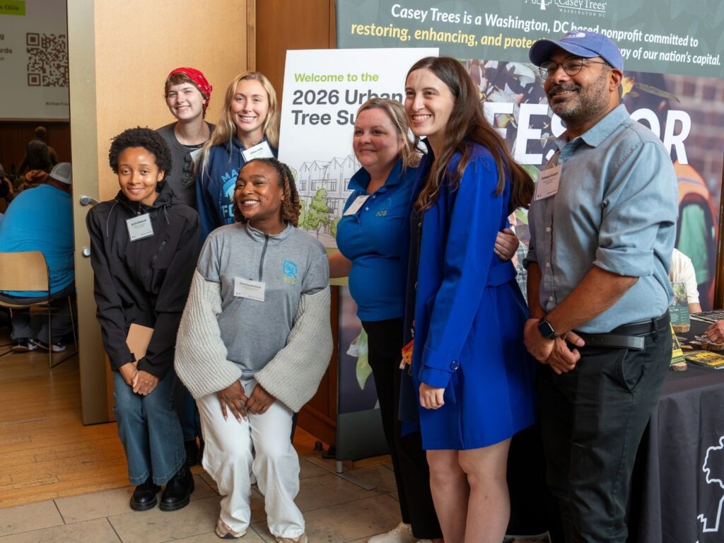 Urban Tree Summit attendees smile in front of an event sign.